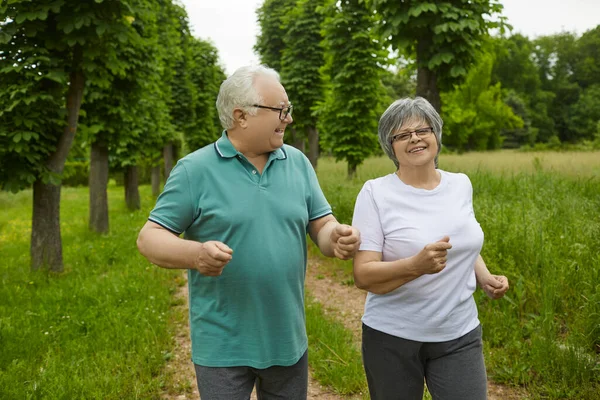 公園や森の中で屋外でジョギング夏の日に幸せなアクティブな高齢者のカップル. — ストック写真