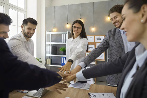 Équipe de gens heureux joignant leurs mains debout autour de la table dans une réunion d'affaires — Photo