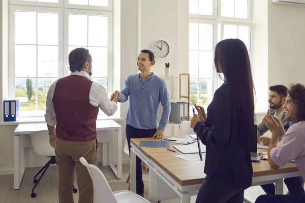 İşletme müdürü genç ve neşeli bir adamla el sıkışıyor ve onu yeni bir takım üyesi olarak selamlıyor..