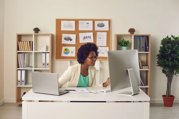 Secrétaire féminine travaillant simultanément sur ordinateur et ordinateur portable assis à son lieu de travail. — Photo