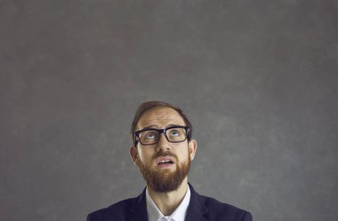 Utangaç iş adamı yüzünde şüpheyle gri bir arkaplana bakıyor..