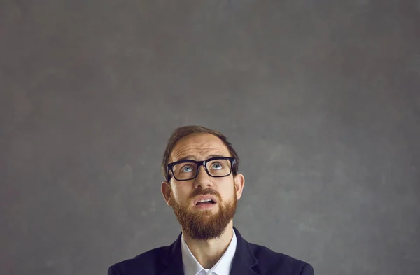 Vernederde zakenman met emotie van twijfel op zijn gezicht kijkend op een grijze achtergrond. — Stockfoto