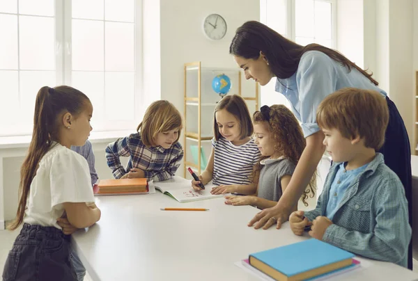 Los niños realizan tareas bajo la supervisión de un maestro de jardín de infantes o un maestro de escuela primaria. —  Fotos de Stock