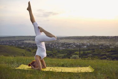 Gün batımında yeşil yaz tarlasında yoga yaparken kadın amuda kalkma egzersizi yapıyor.