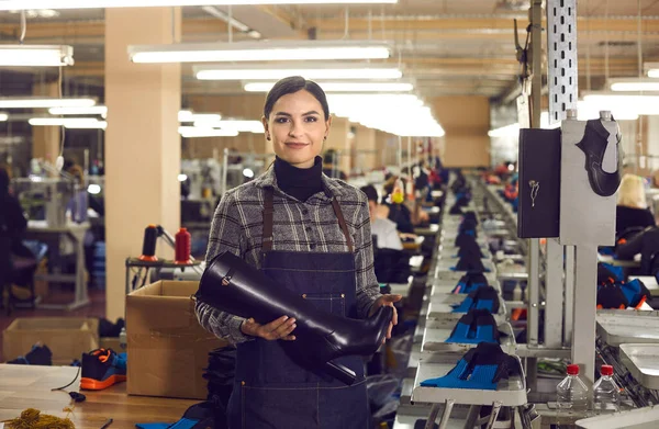 Happy female shoe factory worker holding a womens heeled boot from the new collection.