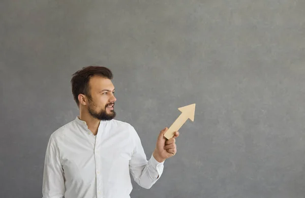 El hombre sostiene una flecha de madera en sus manos, que apunta hacia arriba y simboliza el logro de los objetivos. — Foto de Stock