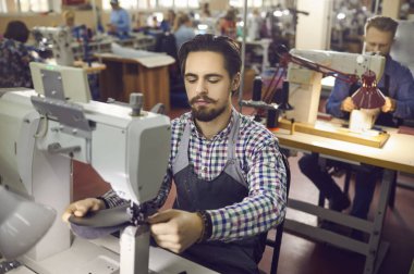 Erkek fabrika işçisi atölyede endüstriyel dikiş makinesiyle masada oturuyor..