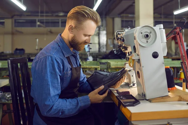 Skilled male employee of a shoe factory checks the quality of mens leather shoes at his workplace.