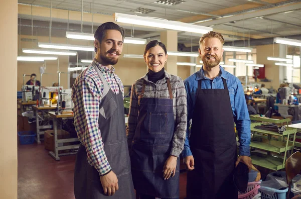 三个快乐的工人站在鞋厂或服装厂车间的画像. — 图库照片