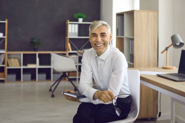 Mutlu yetişkin iş adamının portresi sandalyede oturuyor, gülümsüyor ve kameraya bakıyor.