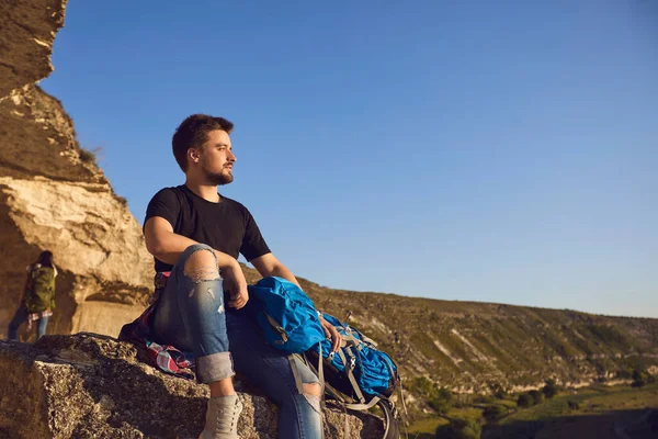 Snílek mladý turista muž sedí na okraji hory a dívá se do dálky. — Stock fotografie