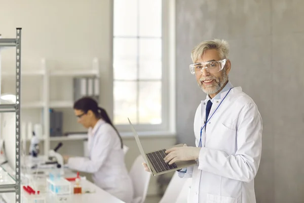 Portret van een arts die in een onderzoekslaboratorium werkt en een laptop in zijn handen houdt. — Stockfoto