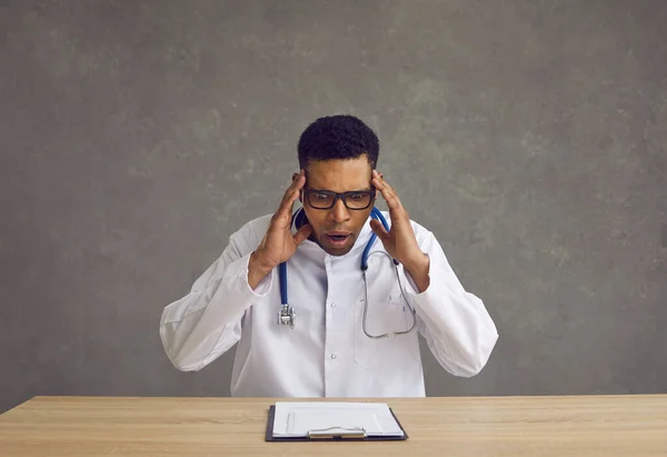 Шокированный молодой африканский американский врач хватает его за голову, читая информацию из буфера обмена. — стоковое фото