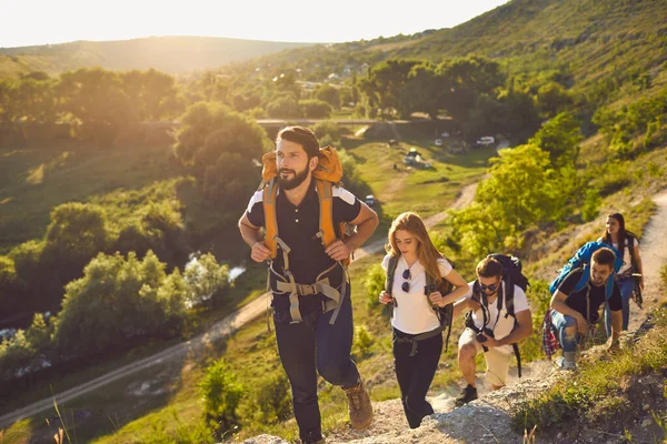 Skupina mladých turistů s batohy na ramenou procházky po skalách na venkově. — Stock fotografie