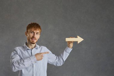 Beyaz bir adam gri arka planda dikilirken yanlamasına ok gösteriyor..