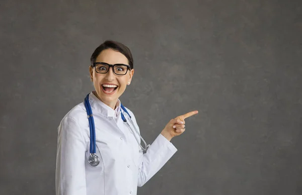 Смешная сумасшедшая женщина-врач, стоящая на сером фоне и улыбающаяся с широко раскрытым ртом и глазами. — стоковое фото