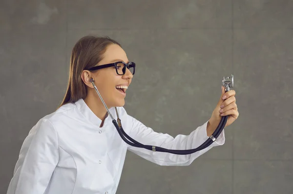Профиль молодой улыбающейся женщины-врача или медсестры, держащей стетоскоп и слушающей. — стоковое фото