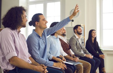 Seyirciler arasında bir adam, bir iş koçuyla yaptığı toplantıda soru sormak için elini kaldırır.