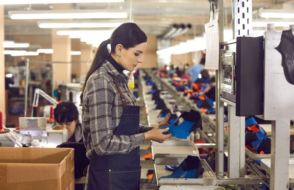 Shoe factory worker standing in sewing workshop and checking quality of sneaker details