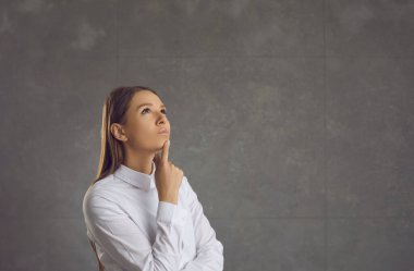 Hayalperest ve düşünceli bir kadının portresi gri bir arka planda düşünceli bir şekilde duruyor..