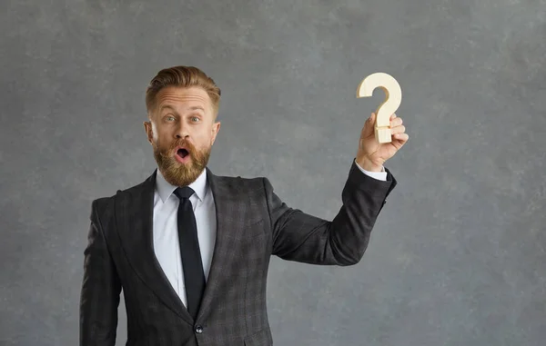 Surprised curious businessman holding question mark standing isolated on grey background — Stock Photo, Image