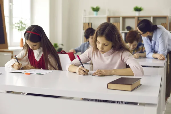 Okos elemi tanuló írás jegyzetfüzetben ül az asztalnál az osztályteremben — Stock Fotó