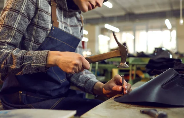 Trabalhador da fábrica de sapatos sentado na mesa de oficina e usando o martelo para fazer botas de couro — Fotografia de Stock