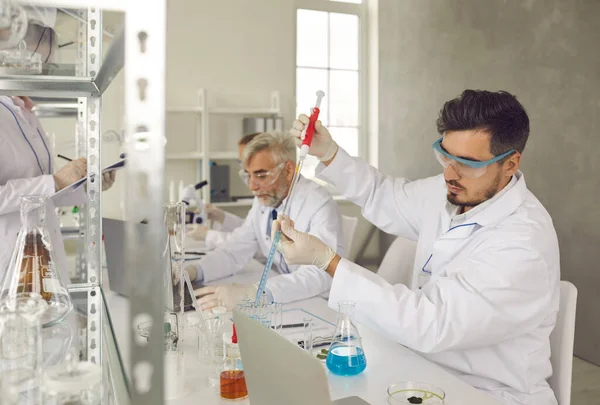Homem cientista colocando amostras de produtos químicos médicos em tubo de ensaio em laboratório — Fotografia de Stock