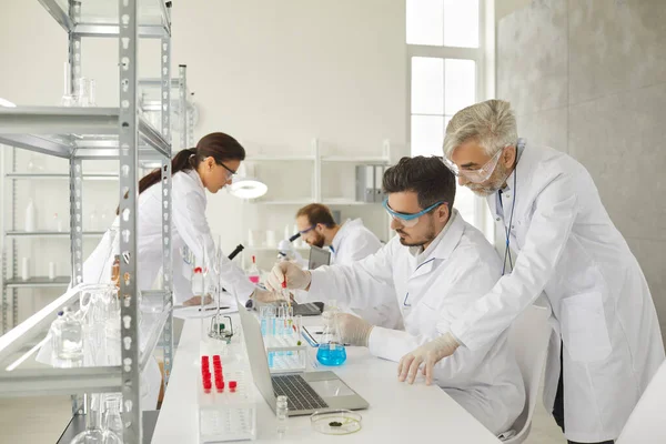 Jonge en oudere volwassen mannelijke onderzoekers werkzaam in modern laboratorium — Stockfoto