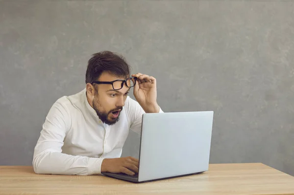 Young man surprised by winning money online looking at screen of laptop computer — ストック写真