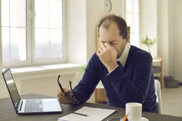 Gammal man som håller glasögon massera näsan känna ögonpåfrestning efter arbete på laptop — Stockfoto