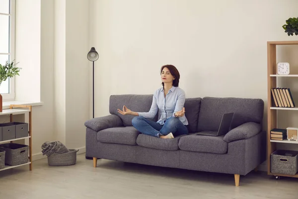 Zakelijke dame die yoga oefeningen doet om stress te verlichten terwijl zij op een bank in lotuspositie zit. — Stockfoto