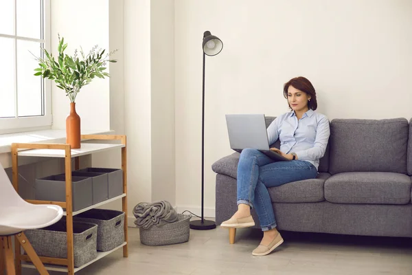 現代の明るいオフィスで快適なソファの上に座ってラップトップで働くカジュアル女性マネージャー. — ストック写真