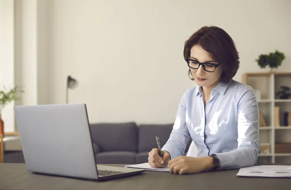 Millennial caucasian woman study on laptop making notes at home office — ストック写真