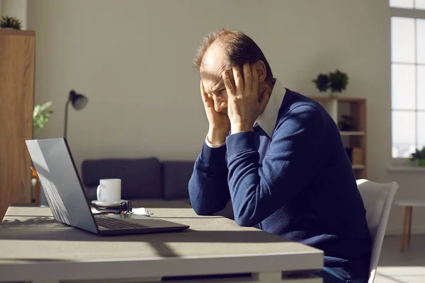 Middle aged man freelancer holding head with hands sitting front of laptop — ストック写真