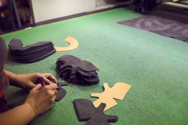 Shoe factory worker making design for new boots standing at table with leather details