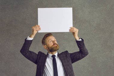 Kafkasyalı işadamı gri bir arka planda kafasının üzerinde beyaz bir kağıt tutuyordu.