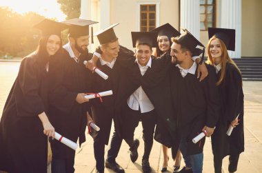 Üniversite binasının arka planında diplomalarla ayakta duran bir grup mutlu mezun.