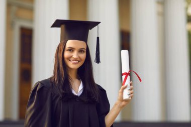 Gülümseyen kız üniversite mezunu elinde diplomayla duruyor.