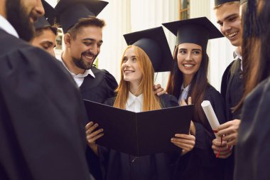 Bir grup gülümseyen üniversite mezunu diplomalarla birlikte mezuniyeti kutluyorlar.