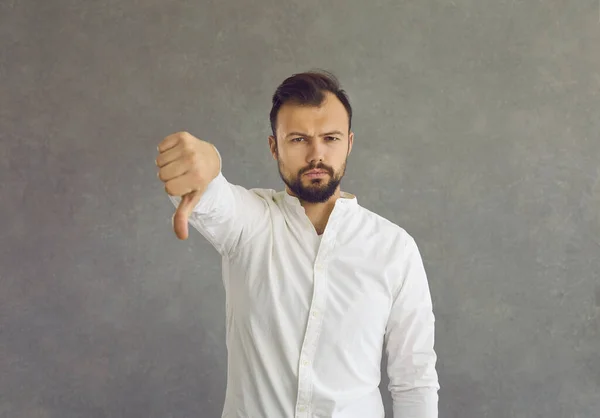 Portret van een jongeman die een duim neerlegt, geïsoleerd op een grijze achtergrond — Stockfoto