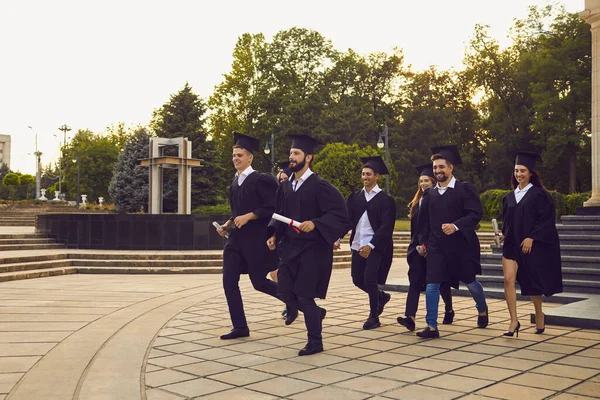 Група веселих випускників університету, які гуляють з димпломами в руках у парку разом — стокове фото