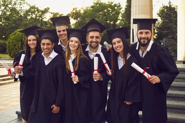 Csoport boldog diplomások séta gödröcskékkel emelt kézzel egyetemi épület háttér — Stock Fotó