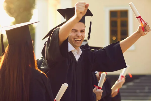 Boldog mosolygós egyetemi diplomás köpenyben tartja diploma emelt kézzel és kifejező boldogság — Stock Fotó