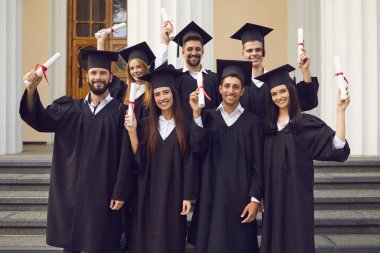 Mezuniyet töreninden sonra ellerinde diplomalarla siyah cüppeli mutlu bir grup mezun.
