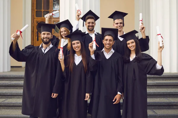 Grupo feliz graduado en túnicas negras con diplomas en las manos después de la ceremonia de graduación — Foto de Stock