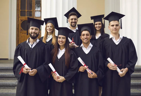 Grupo de estudiantes felices en morteros y vestidos de soltero con diplomas que celebran el éxito. — Foto de Stock