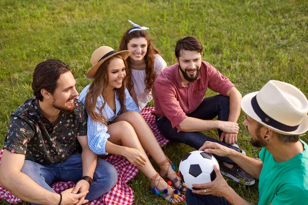 Группа молодых друзей веселятся, сидя на траве и отдыхая в летнем парке. — стоковое фото