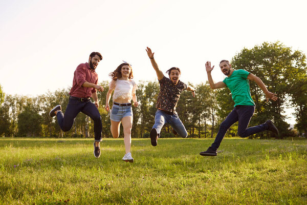 Happy young friends jumping together outdoors. Group of people having fun during summer vacation in countryside