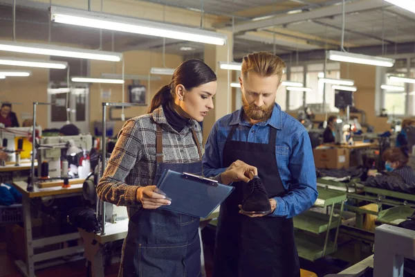 Female master with clipboard checking shoe for defect in shoemaker hands — ストック写真